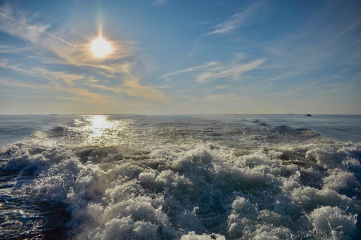 A sunset with boat wake waves behind and the sunlight hitting the water.