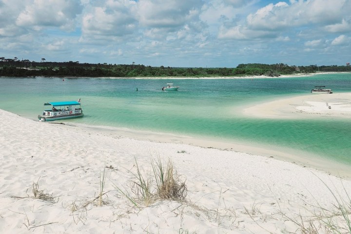 risky Mermaid pontoon boat anchored on white sandbar in Santa Rosa Sound with emerald green water and blue sky near Pensacola Beach