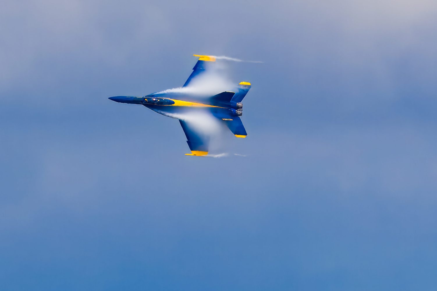Blue Angels jet performing a high-speed maneuver over Pensacola Beach, vapor clouds forming along the wings during a precision flight demonstration.