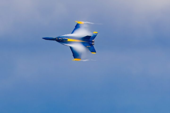 A Blue Angels fighter jet flying through a blue sky with vapor.