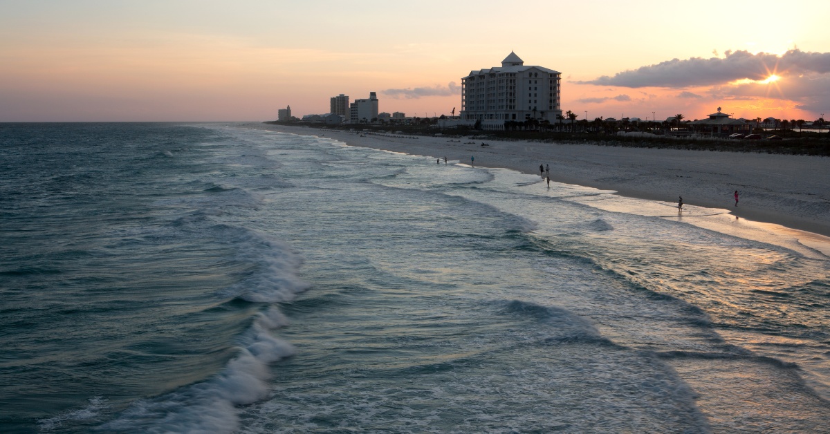 Sunset over a beach with waves and buildings in the distance.
