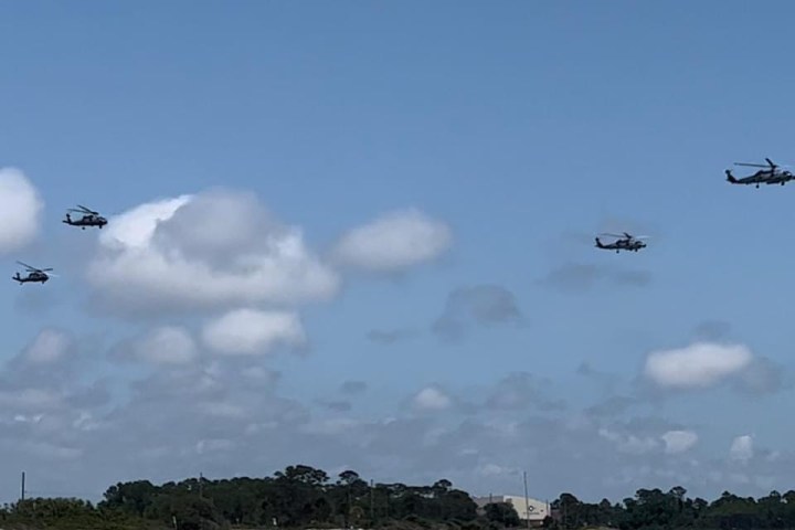 Military helicopters flying in formation over white sand and emerald water near Pensacola Bay during a Frisky Mermaid boat tour.