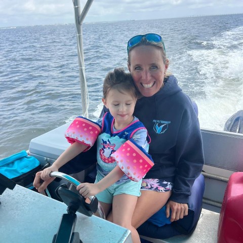 Smiling Frisky Mermaid captain helping a young child hold the boat’s steering wheel during a family-friendly dolphin cruise in Pensacola Bay and the Santa Rosa Sound.