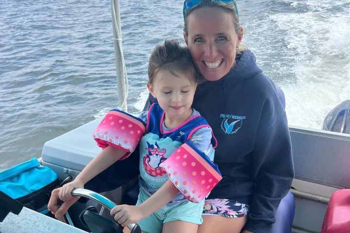 Smiling Frisky Mermaid captain helping a young child hold the boat’s steering wheel during a family-friendly dolphin cruise in Pensacola Bay and the Santa Rosa Sound.