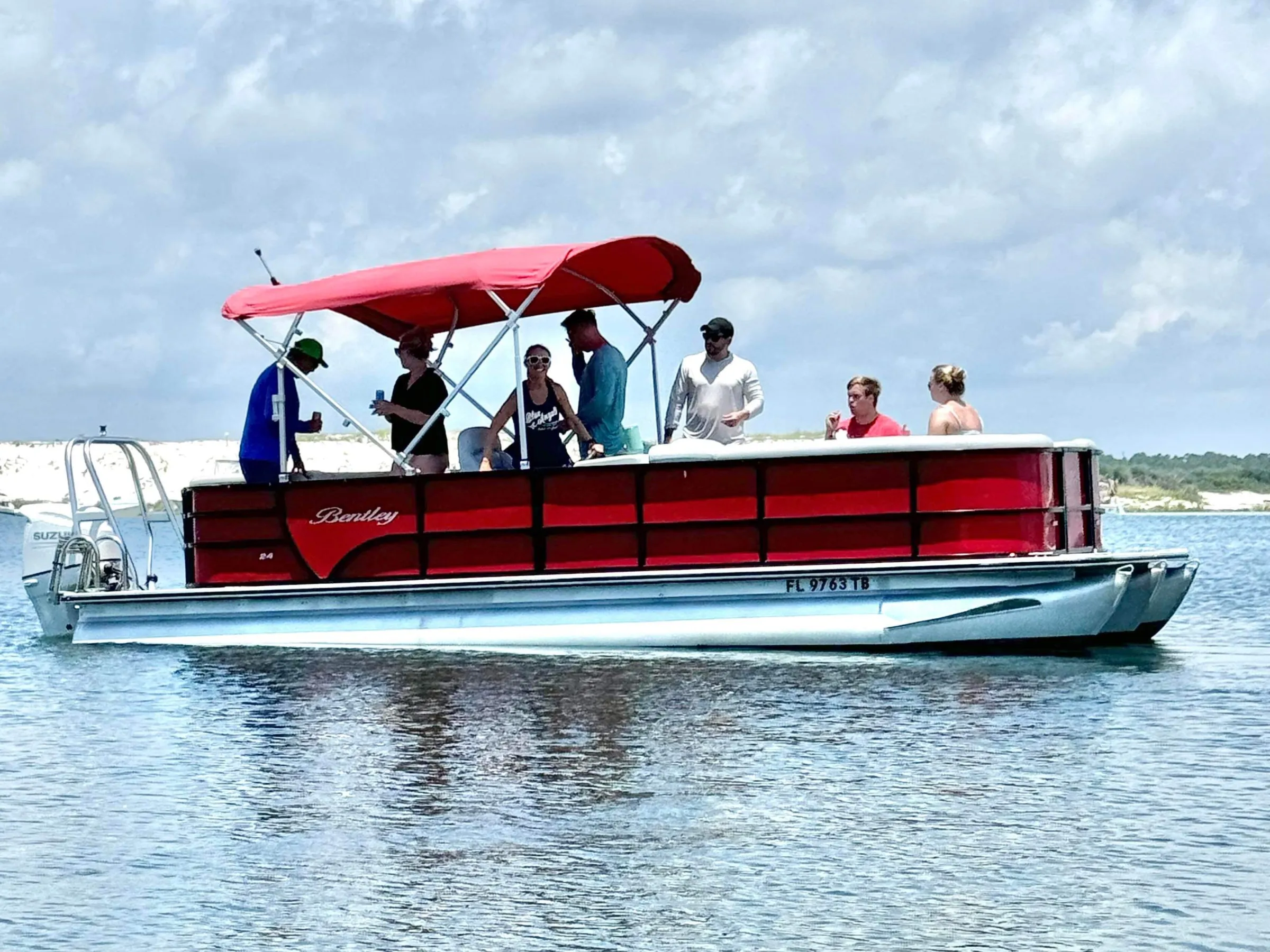 A group of adults enjoying a pontoon boat ride in calm water near Pensacola Beach, Florida, under a bright sky.