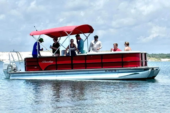A group of adults enjoying a pontoon boat ride in calm water near Pensacola Beach, Florida, under a bright sky.
