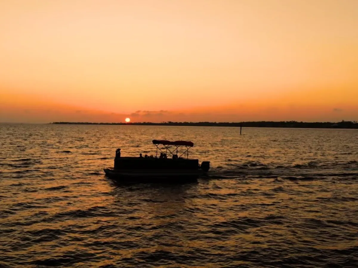 Pontoon boat cruising across the Santa Rosa Sound at sunset near Pensacola Beach, Florida.