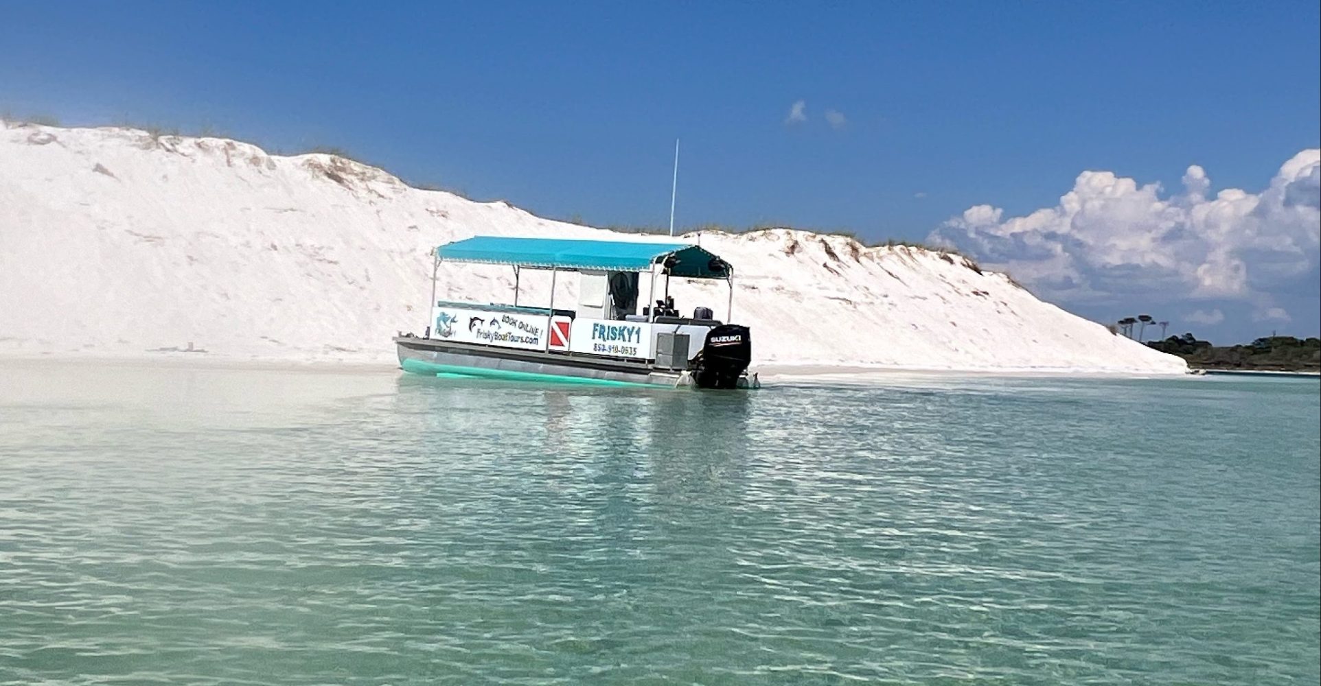 A Frisky Mermaid pontoon boat floating in calm, shallow turquoise water near the white sand dunes of Sand Island in the Santa Rosa Sound by Pensacola Beach.