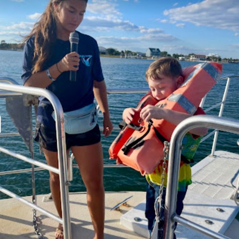 Crew member assists a young child putting on a life jacket aboard a Frisky Mermaid dolphin cruise at Pensacola Beach marina