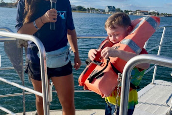 Crew member assists a young child putting on a life jacket aboard a Frisky Mermaid dolphin cruise at Pensacola Beach marina
