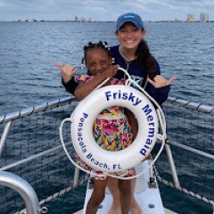 A child and a Frisky Mermaid crew member smile and pose with a life ring on the bow of a dolphin tour boat in Santa Rosa Sound