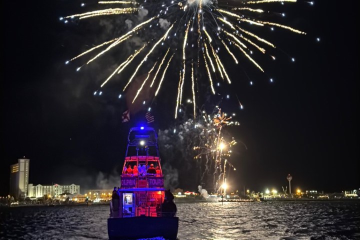 Fireworks exploding over a dolphin cruise boat at night on Pensacola Bay near Pensacola Beach, Florida