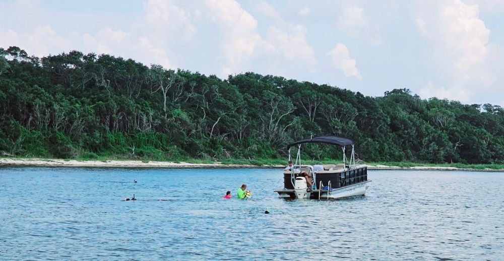 Pontoon boat with family swimming in water nearby.
