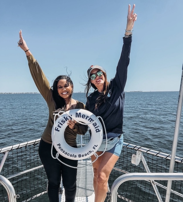 Captain Ally and Shan Bailey with NOLA news now holding a life ring labeled 'Frisky Mermaid', with water in the background.