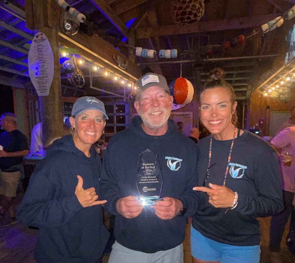 Three people smiling indoors, one holding a trophy, in a casual setting.