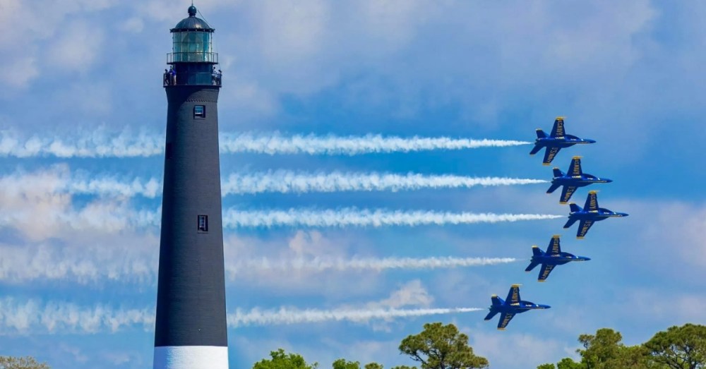 Five jets fly in formation past a tall lighthouse.