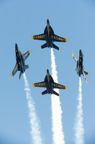 Four Blue Angels flying in formation with vapor trails under blue sky.
