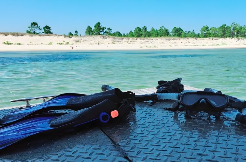 Snorkeling gear on a metal surface by a calm beach with clear blue water.