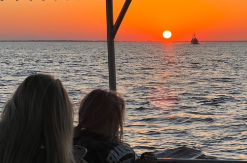 Two people on a boat watching a sunset over the ocean.