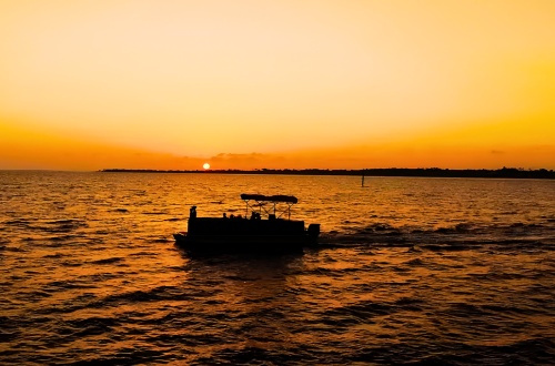 Frisky Mermaid pontoon boat rental on Pensacola Bay at sunset with golden sky reflecting on the water
