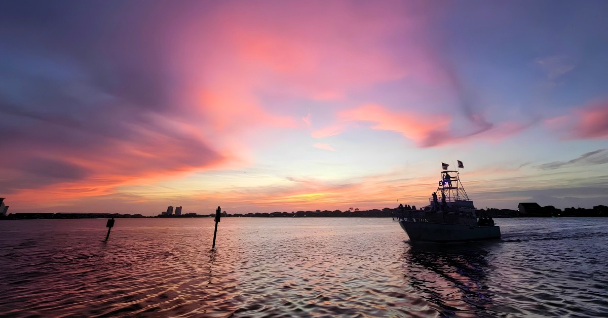 Boat on water at sunset with vibrant pink and purple sky.
